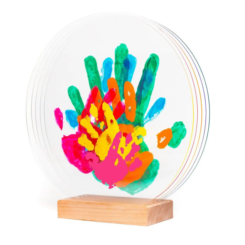 Plaque circulaire transparente avec empreintes de mains multicolores posée sur un socle en bois.